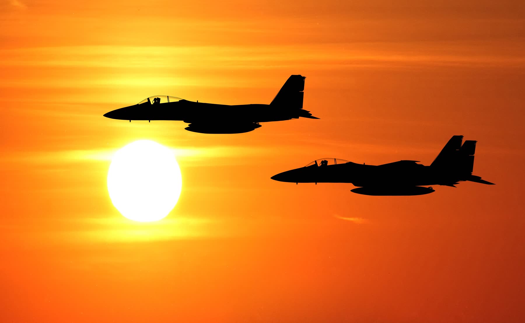 Two fighter jets silhouetted against an orange sun
